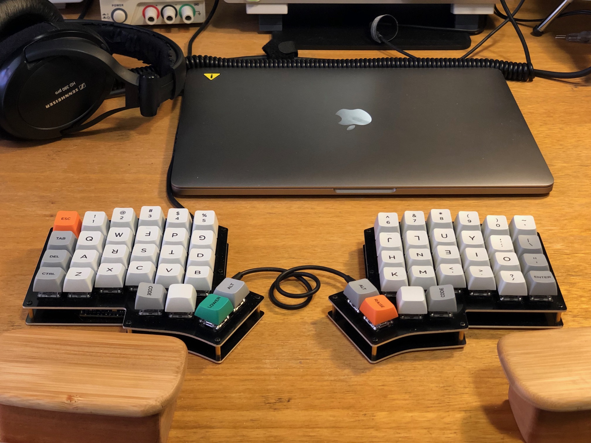 Keyboard on desk with laptop, headphones and wrist rests visible